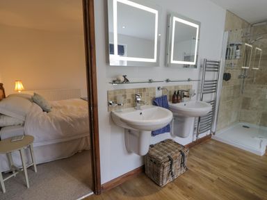 A bathroom with two sinks mirrors and a wicker basket next to a bedroom with a bed and lamp at Pennant Tigi Uchaf in Dinas Mawddwy