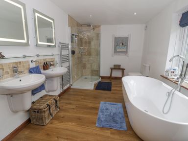 A bathroom with two sinks and mirrors a wicker basket a walk in shower a freestanding bathtub and a toilet at Pennant Tigi Uchaf in Dinas Mawddwy