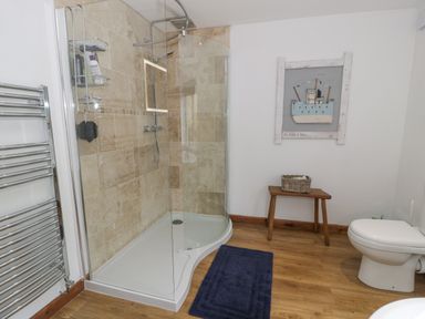 A bathroom with a glass shower enclosure a wooden stool a toilet a blue bath mat and a wall decoration at Pennant Tigi Uchaf in Dinas Mawddwy