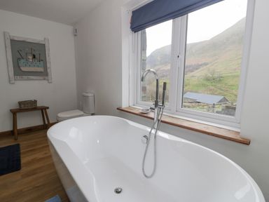 A bathroom with a freestanding bathtub under a window and a toilet next to a wooden bench at Pennant Tigi Uchaf in Dinas Mawddwy