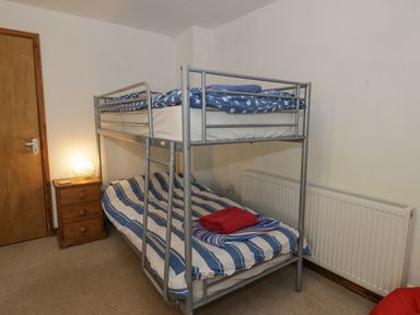 A bedroom with a metal bunk bed with blue and white bedding and a wooden nightstand with a lamp at Pennant Tigi Uchaf in Dinas Mawddwy