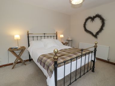 A bedroom with a metal double bed and wooden side tables with lamps at Pennant Tigi Uchaf in Dinas Mawddwy