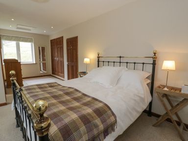 A bedroom with a double bed a plaid blanket bedside tables with lamps a chest of drawers and wooden doors at Pennant Tigi Uchaf in Dinas Mawddwy