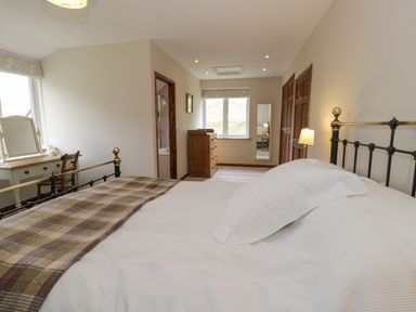 A bedroom with a bed, desk with mirror and chair, dresser, window, and an en suite bathroom at Pennant Tigi Uchaf in Dinas Mawddwy