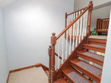 A wooden staircase with carpeted steps and white balusters leading to a carpeted upper floor with a wooden crib at Pennant Tigi Uchaf in Dinas Mawddwy