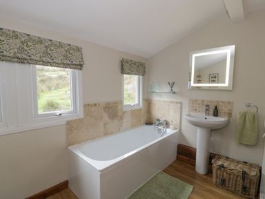 A bathroom with a bathtub sink mirror two windows and a wicker basket at Pennant Tigi Uchaf in Dinas Mawddwy