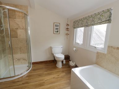 A bathroom with a corner shower, a toilet, a bathtub, and two windows with floral curtains at Pennant Tigi Uchaf in Dinas Mawddwy