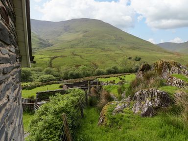 A view of green hills with rocks and a fence beside a stone building at Pennant Tigi Uchaf in Dinas Mawddwy