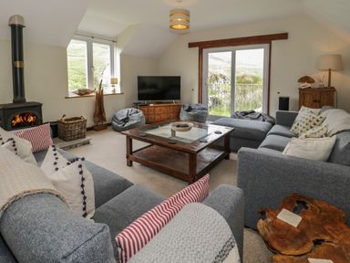 A living room with gray sofas a wood stove a wooden coffee table and a television at Pennant Tigi Uchaf in Dinas Mawddwy