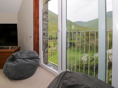 A corner of a room with a television on a wooden stand and bean bags near glass doors overlooking green hills at Pennant Tigi Uchaf in Dinas Mawddwy