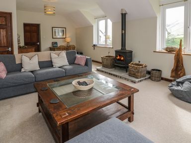 A living room with a gray sofa wooden coffee table and a wood-burning stove at Pennant Tigi Uchaf in Dinas Mawddwy
