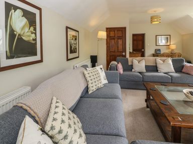 A living room with grey sofas wooden coffee table framed flower pictures and a dining table at Pennant Tigi Uchaf in Dinas Mawddwy