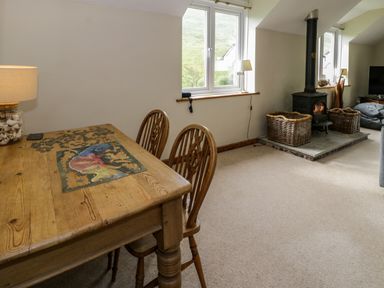 A room with a wooden dining table and chairs a wood stove with two wicker baskets and two windows at Pennant Tigi Uchaf in Dinas Mawddwy