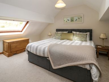 A bedroom with a bed headboard pillows and a throw blanket a wooden chest a window and nightstands with lamps at Pennant Tigi Uchaf in Dinas Mawddwy