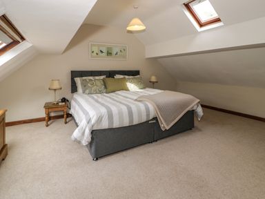 A bedroom with a double bed, bedside tables with lamps, skylight windows, and framed bird artwork at Pennant Tigi Uchaf in Dinas Mawddwy