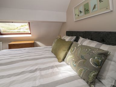 A bedroom with a bed with striped bedding and decorative pillows underneath a window at Pennant Tigi Uchaf in Dinas Mawddwy