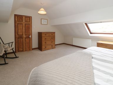 A bedroom with a wooden door a wooden chest of drawers a black rocking chair and a bed near a skylight window at Pennant Tigi Uchaf in Dinas Mawddwy