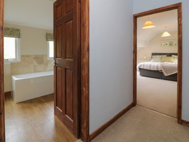 A hallway with two doorways showing a bathroom with bathtub and a bedroom with bed at Pennant Tigi Uchaf in Dinas Mawddwy