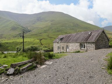 A stone house with a gravel driveway near green hills and a utility pole at Pennant Tigi Uchaf in Dinas Mawddwy