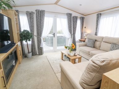 A living room with a beige sofa a television and a coffee table with flowers at Chantry Lodge in Hendra Croft near Goonhavern