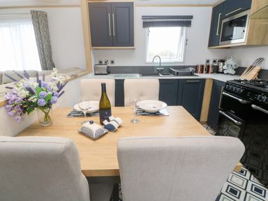 A kitchen with a dining table set with plates and wine glasses next to blue cabinets at Chantry Lodge in Hendra Croft near Goonhavern