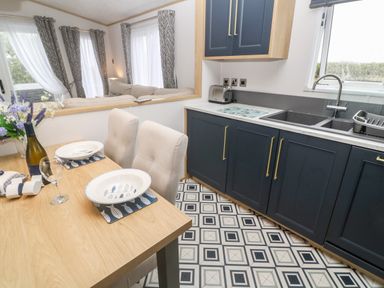 A kitchen and dining area with wooden table, beige chairs, blue cabinets, and patterned floor at Chantry Lodge in Hendra Croft near Goonhavern