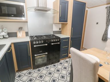 A kitchen with dark blue cabinets a black stove a microwave and a dining table with chairs at Chantry Lodge in Hendra Croft near Goonhavern