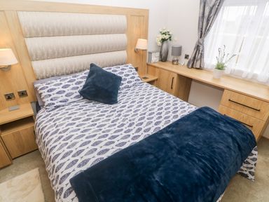 A bedroom with a bed with patterned bedding and a blue throw at Chantry Lodge Hendra Croft near Goonhavern