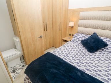 A bedroom with a bed a bedside table with a lamp built in wardrobes and a visible toilet at Chantry Lodge in Hendra Croft near Goonhavern