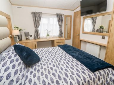 A bedroom with a bed a desk below a window and a wall mounted TV at Chantry Lodge in Hendra Croft near Goonhavern