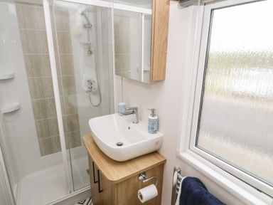 A bathroom with a shower enclosure sink with faucet and cabinet a mirror a window and a towel on a radiator at Chantry Lodge in Hendra Croft near Goonhavern