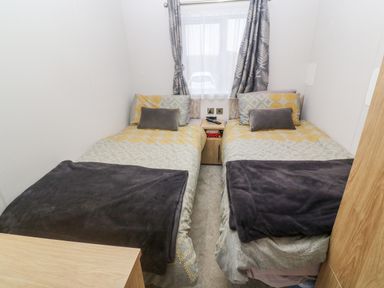 A bedroom with two single beds a window between them and curtains at Chantry Lodge Hendra Croft near Goonhavern