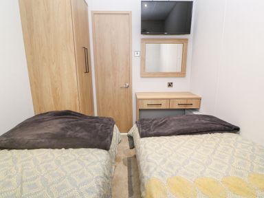 A bedroom with two single beds a wooden wardrobe a wooden door a wall-mounted TV a wooden desk with drawers and a mirror Chantry Lodge Hendra Croft near Goonhavern