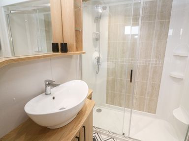 A bathroom with a white basin on a wooden countertop and a glass-enclosed shower at Chantry Lodge in Hendra Croft near Goonhavern