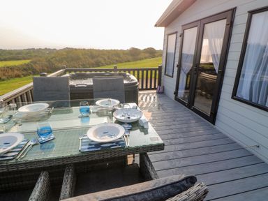 An outdoor deck with a glass dining table set for four and a hot tub at Chantry Lodge in Hendra Croft near Goonhavern