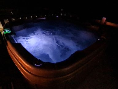 An illuminated hot tub with bubbling water at night at Chantry Lodge in Hendra Croft near Goonhavern