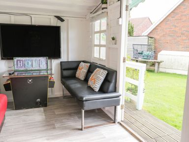 A room with a black sofa and two pillows a large television on the wall a sign that reads home and a door opening to a garden at Wyvill House in Cayton