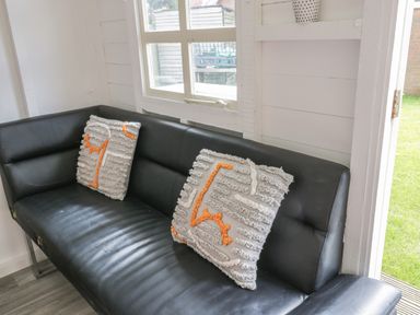 A black leather sofa with two decorative cushions near a window and an open door showing a grassy area at Wyvill House in Cayton