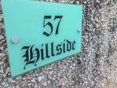 A green house number sign 57 Hillside mounted on a pebble textured wall at Hillside in Gunnislake