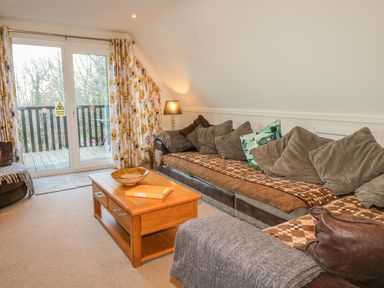 A living room with a brown sofa and cushions a wooden coffee table and glass doors leading to a balcony at Hillside in Gunnislake