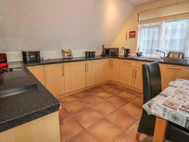 A kitchen with wooden cabinets black countertops tiled floor and a dining table with chairs at Hillside in Gunnislake