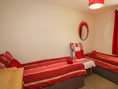 A bedroom with two single beds a chair a round mirror and red curtains at Hillside in Gunnislake