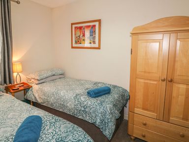 A bedroom with two single beds a wooden wardrobe a nightstand with a lamp and a framed picture on the wall at Hillside in Gunnislake