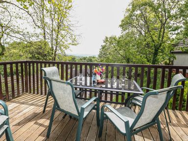 An outdoor wooden deck with a table glass top and four chairs surrounded by trees at Hillside in Gunnislake