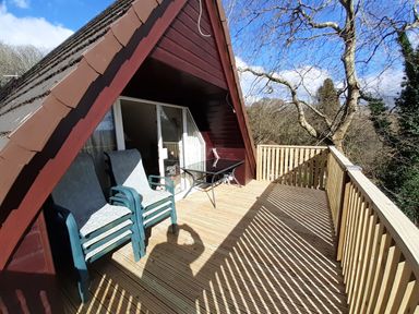 A balcony with two chairs and a table attached to a wooden house with a sloped roof at Hillside in Gunnislake