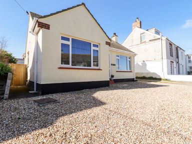 A single story house with large windows and a gravel driveway at Seawynds in Crantock