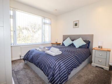 A bedroom with a double bed with striped bedding and two bedside tables with lamps at Seawynds in Crantock