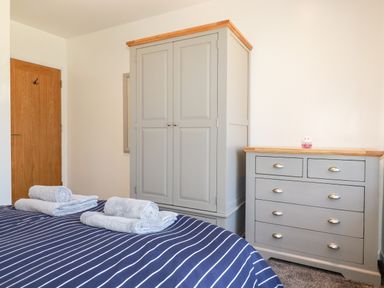 A bedroom with a bed with striped bedding and folded towels a wardrobe and a chest of drawers at Seawynds in Crantock