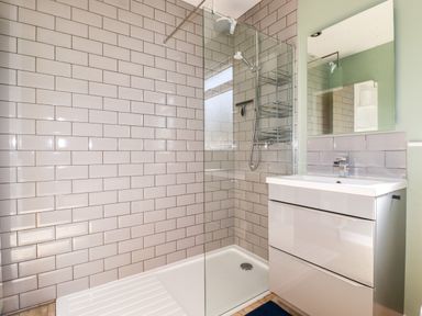 A bathroom with a walk-in shower with glass panel and a sink with cabinet under a mirror at Seawynds in Crantock