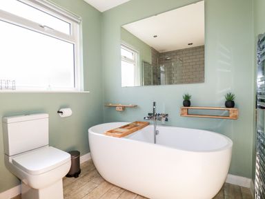 A bathroom with a freestanding bathtub a toilet a window and a large mirror at Seawynds in Crantock